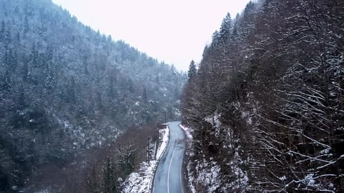 Aerial View of Snowy Mountain Road Through Winter Forest and River Valley