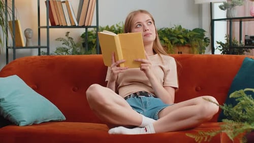 Junge Frau liest interessantes Buch, blättert lächelnd, genießt Literatur und ruht sich auf der Couch aus
