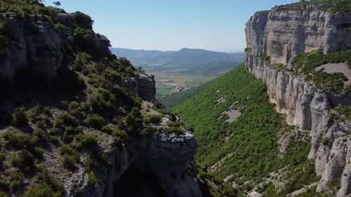 Aerial image of a large canyon, with green tones and a lush forest, as well as large rock walls. It