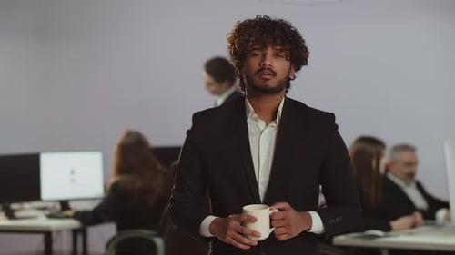 Video with a Tired Young Man in a Formal Suit Standing Against the Backdrop of the Office View of a