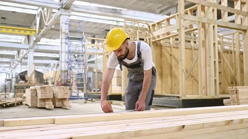 Debout, marquant la planche au crayon. Ouvrier industriel dans un entrepôt en bois.