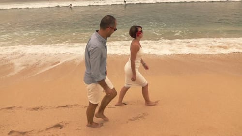 Elegant young couple walking on sandy beach by the sea in super slow motion