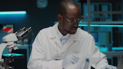 Scientist Analyzes Samples Using Microscope and Laptop