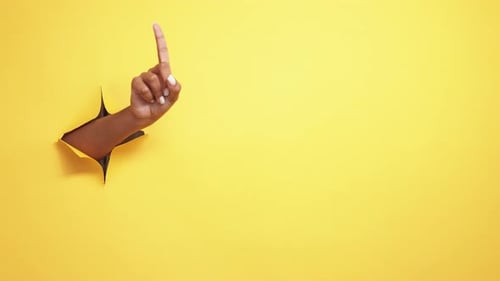 Hand Poking Through Hole Pointing Upward on Yellow