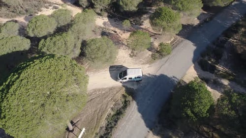 White campervan reversing from a gravel road into main asphalt road in a forest