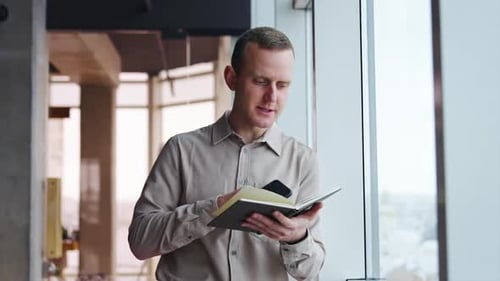 Man Writing in Notebook with Phone in Office