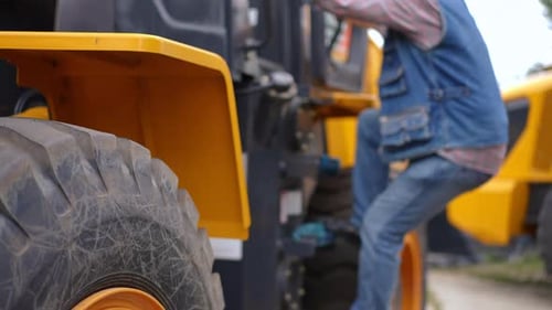 Senior Farmer Climbing Down from a Yellow Tractor