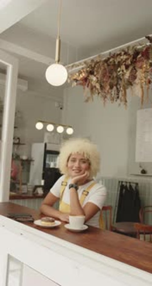 Vertical video: Woman in cafe smiling, sitting at counter with coffee and donut