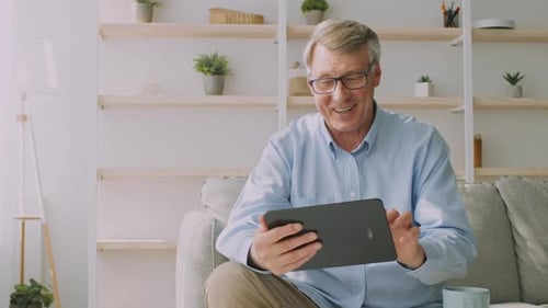 Senior Man Using Tablet Device on Couch at Home