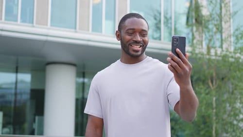 African American Man Holding Smartphone Having Video Chat on Urban Street in City Guy Blogger