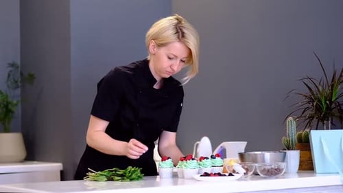 Woman Decorates Cupcakes with Berries and Greenery