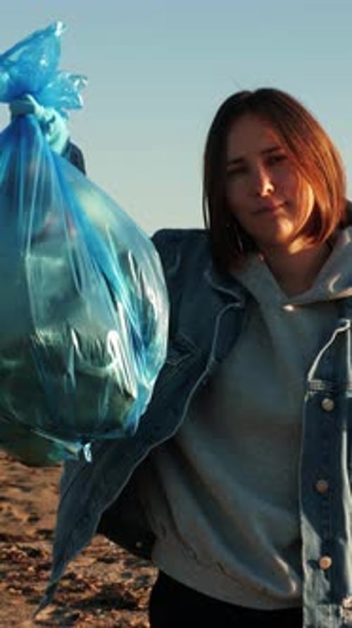 Mujer que sostiene una bolsa de basura llena de botellas de plástico y basura. Vídeo vertical