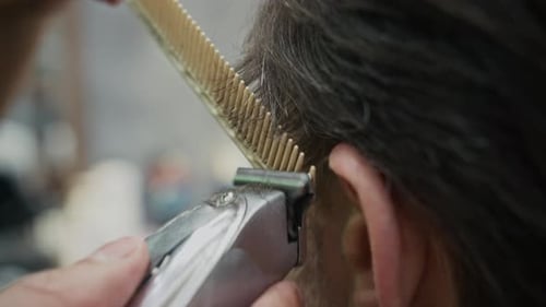 Friseur schneidet die Haare eines männlichen Kunden mit Haarschneidemaschine und Kamm