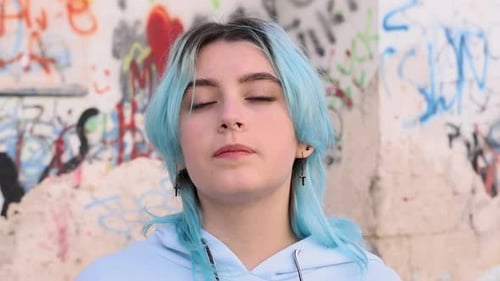 Blauhaariges Teenager-Mädchen im hellblauen Hoodie vor der Graffiti-Wand. Kopf-Porträt