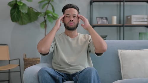 Man Massaging Temples on Sofa Indoors