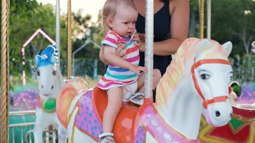Baby Rides Carousel Horse with Mother in Urban Park