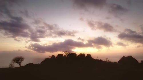 The sky is painted in soft pastel hues as the sun sets behind a silhouette of rocky terrain and spar