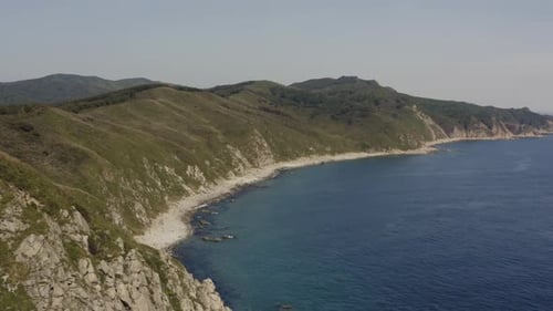 Fly over steep cliff coastline with deep blue ocean on a clear sunny day. Russia Far East. Aerial sh