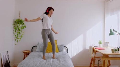 Joyful Young Teenage Girl Listening to Music with Headphones Dancing on Bed
