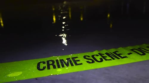 Crime Scene tape abandoned on wet concrete ground while rain falls on it, night time in slow motion.