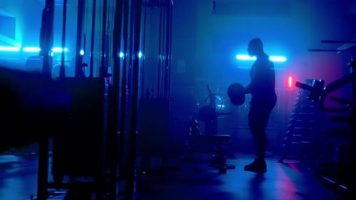 Side View of Dark Silhouette of Bodybuilder is Pumping His Arms with Barbell