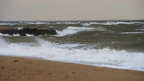 Choppy Waves Crash Against Rocky Breakwater on Sandy Shoreline Raw Power of Nature Stormy Sea