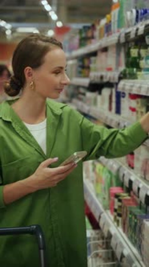 Vertical Video Woman Choosing Cosmetics Using Smartphone in Supermarket