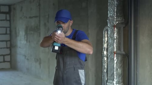 Maintenance Worker in Uniform Holds a Screwdriver and Looks at the Camera Against the Background of