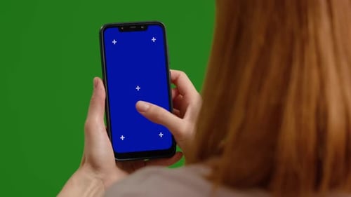 Female scrolls blue chroma key screen phone and likes posts on green screen background.