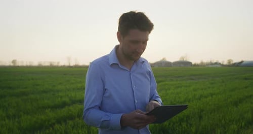 Man with Tablet Smiling in Rural Field at Sunset