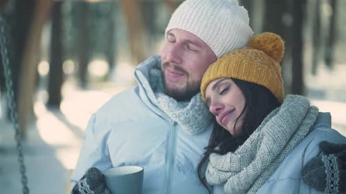 Young Couple Relax in a Winter Forest a Man and a Young Woman Sit on a Swing and Ride While Relaxing