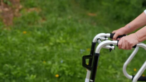 Closeup of an Elderly Woman's Hands Gripping a Walker in a Green Park Emphasizing Support and