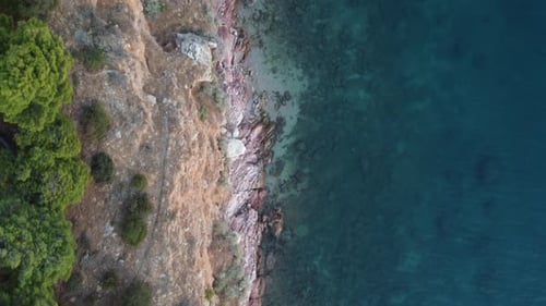 Top view of a cliff with rugged and dramatic coastline next to deep blue sea | 4K