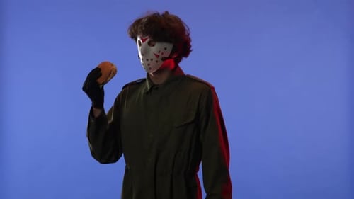 Man in White Mask Sniffing Burger and Showing OK Gesture on Blue Background with Red Neon Light