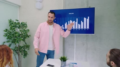 A Male Analyst is Giving a Presentation to a Group of Economists in a Meeting Room at Office He is