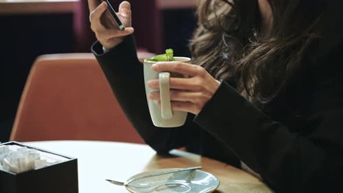 Caucasian Female Sitting Inside of Modern Cafe with a Lot of Green Plants Drinking Hot Tea with Mint