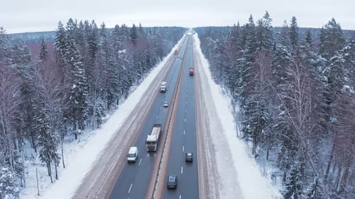 Cars drive along the highway among snow-covered trees and roadsides