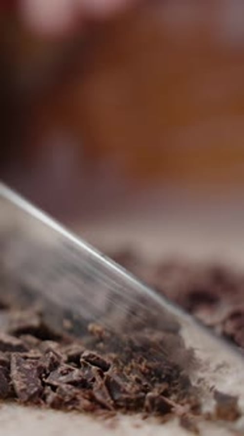 Vertical video. Macro Shot Of Chocolate Being Chopped With A Knife. Slow Motion.