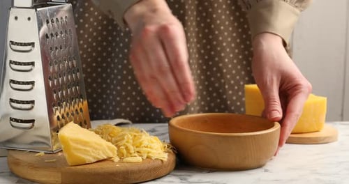 Woman putting grated cheese into bowl at white marble table, closeup