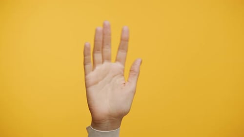 Hand Waving Against Yellow Background