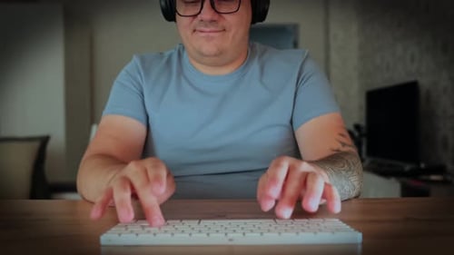 Cheerful guy with tattooed hands is typing on modern keyboard, dark vignette, close up.