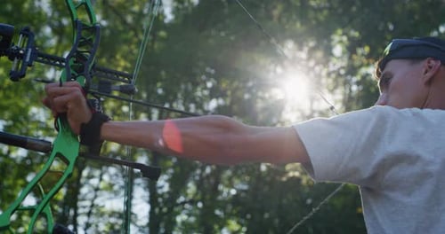 Slow motion close up of young man with professional equipment is practising archery with a bow in
