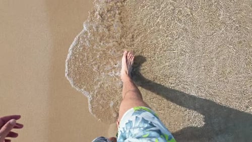Man walking on sandy beach, waves gently touching his feet in a peaceful moment
