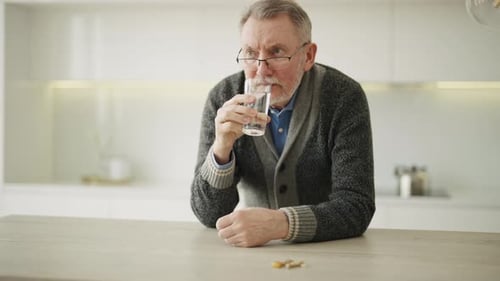 Senior Man Drinks Water with Pills in Kitchen
