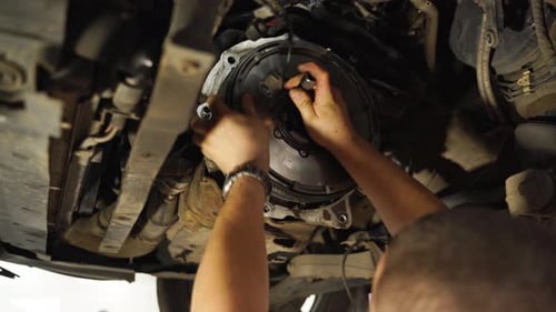 Un mécanicien automobile installe un ensemble d'embrayage dans le dessous du véhicule, les mains naviguent avec expertise sur le volant