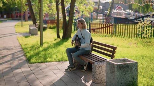 Relaxed Street Musician Playing Acoustic Guitar Amidst City Scenery Serene Outdoor Artist Composing