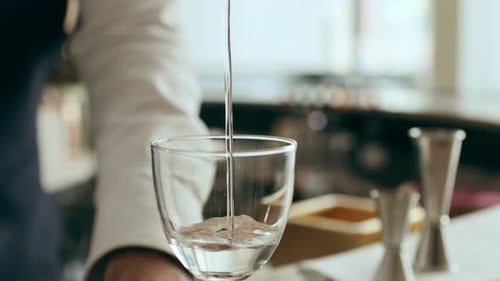 Bartender prepares a cocktail, filling glass with liquid