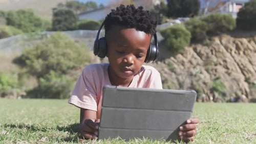 Using tablet and wearing headphones, boy studying outdoors for school