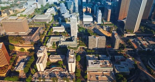 Rising above sunlit Los Angeles downtown. Crazy traffic on the roads of metropolis from aerial view.