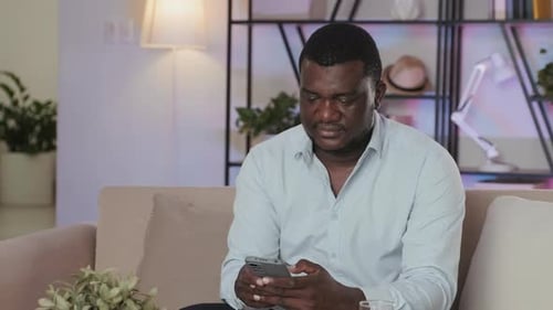 Man Sitting on Sofa Using Smartphone Indoors